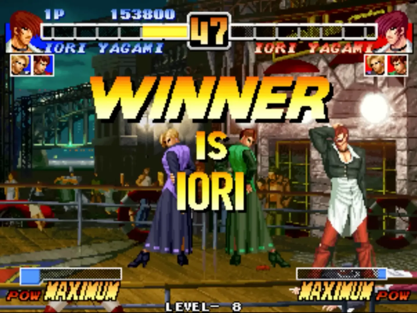 Iori Yagami grabbing his face and maniacally laughing during his intro pose, his crimson hair contrasting sharply with the dim stage lighting.