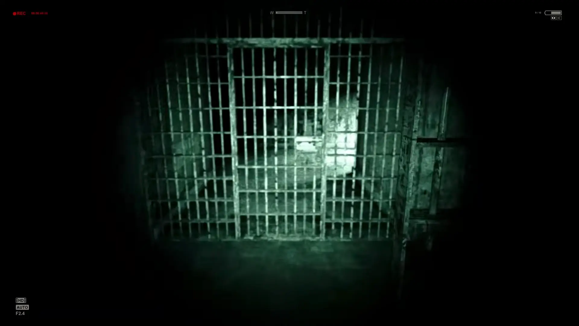 A deeply unsettling shot of a ruined cell block viewed entirely through the grainy green night vision of the camcorder.